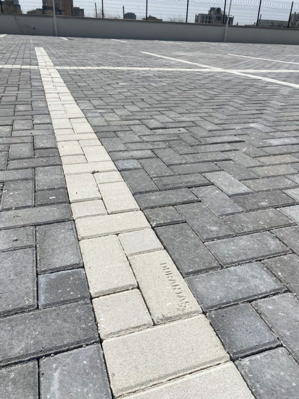 Gri parke taşı zeminde açık renk taşlarla oluşturulmuş yönlendirme şeridi