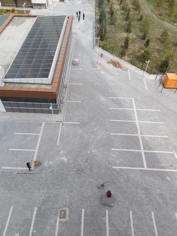 Kuşbakışı otopark alanında kilit taşı döşeme, rögar kapakları ve park çizgileri